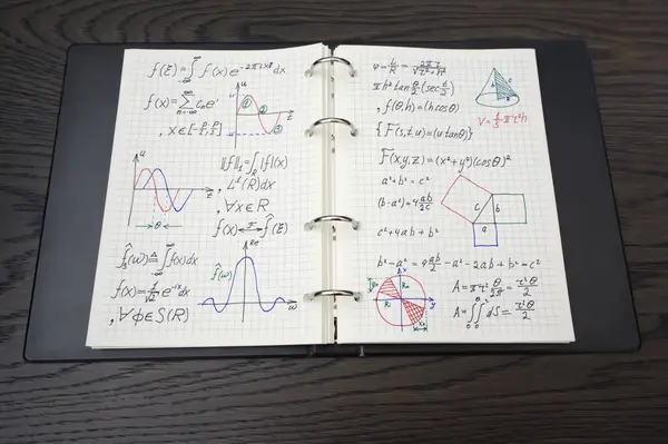 Resim, karmaşık matematiksel denklemler ve renkli grafiklerle dolu bir defter gösteriyor, matematikte gelişmiş çalışmanın göstergesi, koyu ahşap bir yüzeye yerleştirilmiş..