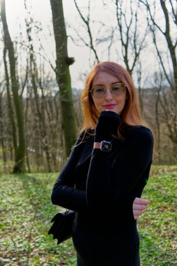 Siyah bir kıyafet giymiş bir kişi ormanda duruyor; doğal zemin koyu renk kıyafetle çelişiyor.. 