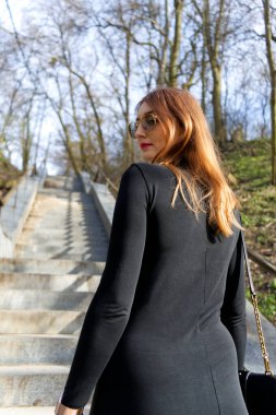 Yoğun ve karanlık bir ormana giden eski bir taş merdivenin önünde gizemli bir figür duruyor. Ağaçların arasında sis örüyor, ürkütücü ama büyüleyici bir atmosfer yaratıyor.. 