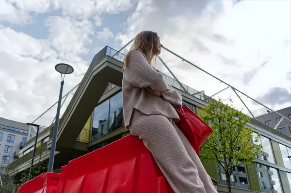  Dalgın bir kadın canlı kırmızı bir merdivende, şehir zeminine karşı oturur. Parçalı bulutlu bir gökyüzünün altında çarpıcı bir kontrast yaratır..