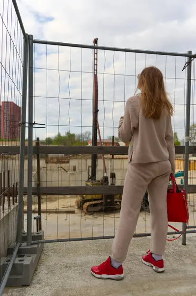 Stock image  A person observes the progress of an urban construction site from behind a safety fence, highlighting the juxtaposition of daily life and development.