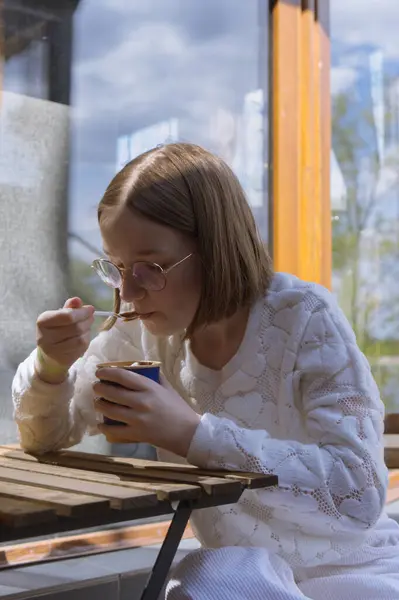 Sade beyaz örgü süveter giyen biri ahşap bir masada içki içmekten hoşlanır.
