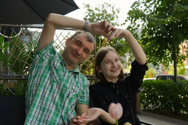 Baba ve kızı açık bir kafe masasında oturup elleriyle kalp şekilleri oluşturuyorlar.. 