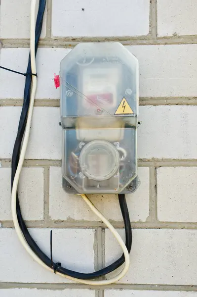 Görüntü, bir mülkün elektrik tüketimini ölçtüğünü gösteren, kablolu bir duvara bağlı bir elektrik sayacı gösteriyor..