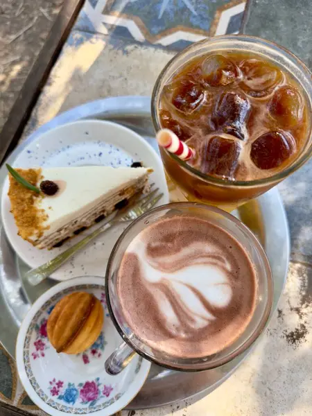 Serinletici buzlu bir kahve, karışık latte sanatıyla sıcak bir kahve, bir dilim katmanlı kek ve masadaki küçük bir pasta, rahatlatıcı bir ikindi ikramı için mükemmel..