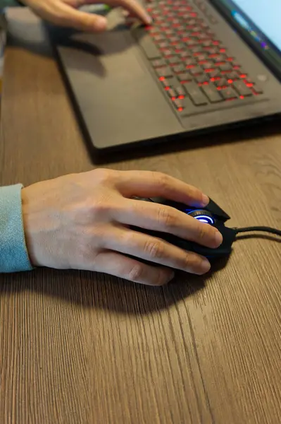 Bir kişi kırmızı arka planda klavyesi olan bir dizüstü bilgisayar üzerinde çalışırken parlayan mavi kaydırma tekerleği olan kablo bir bilgisayar faresi kullanıyor..