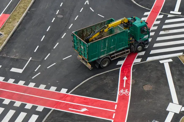 Yeşil bir kamyon işaretli bisiklet yolları ve yaya geçitleri olan bir kavşakta..