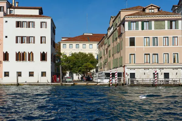 Renkli binalar, merkezi bir ağaç ve sakin bir yansıması olan, Avrupa şehrinin, muhtemelen Venedik 'in, ikonik su yollarıyla cazibesini gözler önüne seren pitoresk bir kanal sahnesi..