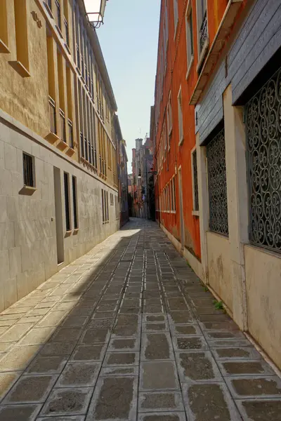 Açık gökyüzünün altındaki kırmızı ve sarı binalar arasında dar, kaldırımlı bir ara sokak. Bakış açısı uzak bir noktaya götürüyor. Venedik 'in bu tarihi caddesinde cazibe ve sükuneti çağrıştırıyor..