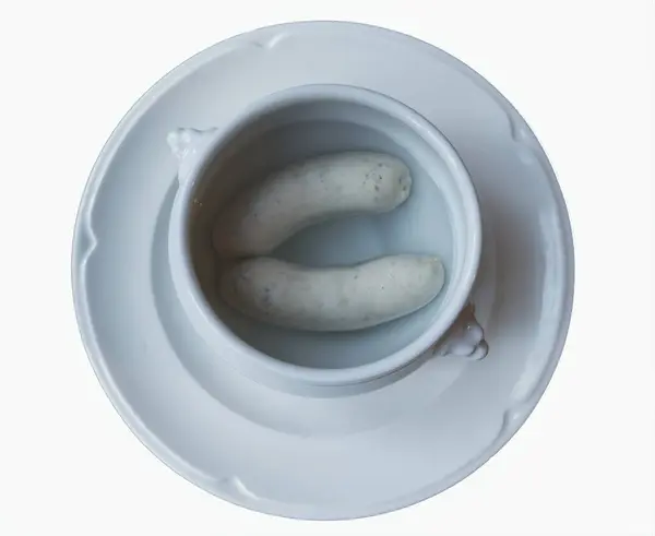 Resim, beyaz bir tabağa yerleştirilmiş suyla dolu beyaz bir kasede iki beyaz sosisi gösteriyor. Basitlik ve monokromatik renk düzeni bunu görsel olarak çarpıcı ve ilgi çekici kılıyor..