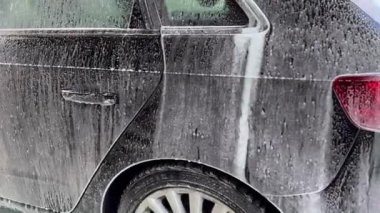 Araba yıkama sırasında damlayan sabun köpüğüyle kaplı bir araba. Kalıplı sabun deseni görsel olarak çekici bir sahne yaratıyor..