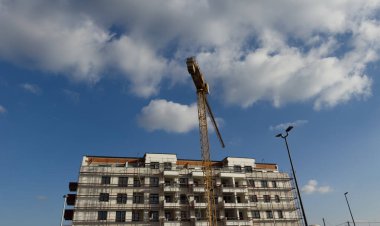 Görüntü inşaat halindeki bir inşaat alanını ve önünde uzun sarı bir vinç olduğunu gösteriyor.. 