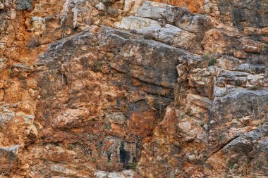 Kahverengi, turuncu ve gri tonlarında, detaylı dokular, katmanlar ve jeolojik oluşumlar gösteren kayalık bir uçurumun yakın görüntüsü. Erozyon ve yıpranmayla şekillendirilmiş doğal bir başyapıt..