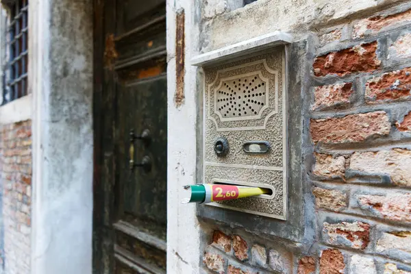 Yıpranmış bir Venedik duvarında, sarılmış kağıt etiketli eski bir posta kutusu var..