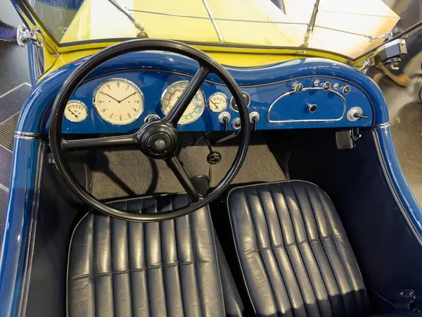 Modası geçmiş mavi bir arabanın içinde, göstergeleri, direksiyonu ve lüks deri koltuklarıyla gösterge paneline odaklanan yakın plan bir görüntü. Klasik tasarım ve titiz detaylar çok açık.
