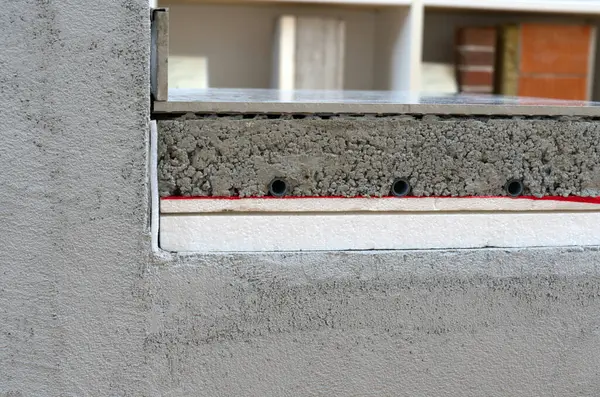 Kesme bir görüntü, inşaat veya yenileme işlemi sırasında beton, yalıtım ve radyan ısıtma boruları da dahil olmak üzere bir binanın yapısının katmanlarını gösteriyor.