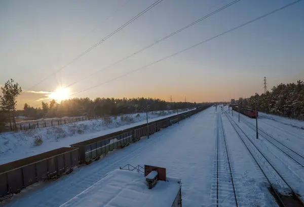 Railway junction of freight trains among forests under snow at sunset.Freight trains standing on rails among snow-covered forests, all illuminated by the setting sun.