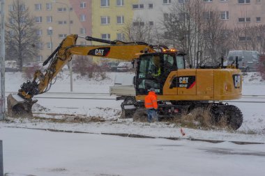 Polonya Ostrowiec Swietokrzyski, 28 Kasım 2024 saat 14: 36 'da kar yağışı sırasında toprak çalışmalarını gerçekleştirir. Bir operatör yansıtıcı giysiler giyen bir işçiyle görüşür. Bir işçi yolu özel bir ekipmanla temizler. .