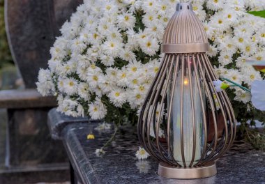  All Saints Day - flowers and burning candles on a granite tomb. A beautifully decorated grave on the occasion of All Souls Day. A burning candle expressing memory of the deceased and hope that he was saved and is in heaven. 