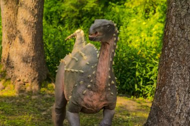 Polonya Baltow 30 Mayıs 2023, saat 15: 47. İlkbaharda ağaçların arasında bir Scelidosaurus. Bir otobur dinozor, bir Mayıs öğleden sonra merakla etrafına bakar. Jura Park, paleontolojik cazibeler parkı. Ormandaki dinozor.  