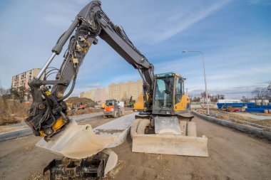 Polonya Ostrowiec Swietokrzyski 24 Şubat 2024 saat 15: 00 'te. Bir yol inşaatında volvo kazıcı. Mavi gökyüzünün altında beyaz bulutlu bir yol inşaatında kazıcı. .