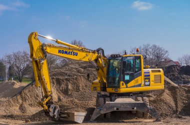 Kumda kazıcı. Polonya Ostrowiec Swietokrzyski 8 Mart 2024 saat 12: 00 'de. Komatsu kazıcısının yanında çakıl yığını var. Japon tekerlekli kazıcı, tam bahar güneşinde bir kova dolusu çakılla hidrolik desteklerin üzerinde duruyor. .  