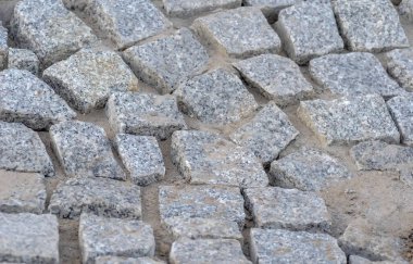 Taş kaldırım arka planı. Çakıl taşlarının dokusu. Granit kaldırım taşlarından yapılmış bir asma. Lağım kanalizasyonunun etrafındaki baca yamaçtaki kaldırımın yanındaki granitle döşenmiş.. 