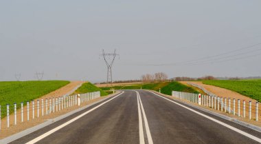 Şehirdeki yol. Bulutlu bir gökyüzünün altında şehir dışındaki yol. İlkbaharın başlarında tarlalarda (tarımsal bir alanda) akan eğri bir yol.