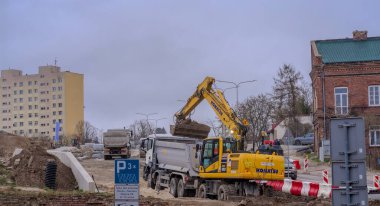 Bir şehirde inşaat alanı. Polonya Ostrowiec Swietokrzyski 18 Mart 2024, saat 12: 30. Yağmurlu bir günde bir yol inşaatında Komatsu kazıcısı. Bulutlu grimsi gökyüzünün altındaki bir yol inşaatı sırasında Japon tekerli kazı aracı.  