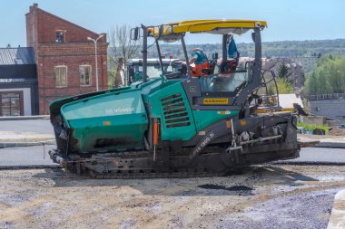 The road is working.Poland Ostrowiec Swietokrzyski April 12 at 12:14. Vogele - asphalting machine in action. Asphalting the surface of a newly built road in the city among the historic urban buildings.  clipart
