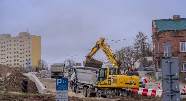 Bir şehirde inşaat alanı. Polonya Ostrowiec Swietokrzyski 18 Mart 2024, saat 12: 30. Yağmurlu bir günde bir yol inşaatında Komatsu kazıcısı. Bulutlu grimsi gökyüzünün altındaki bir yol inşaatı sırasında Japon tekerli kazı aracı.  