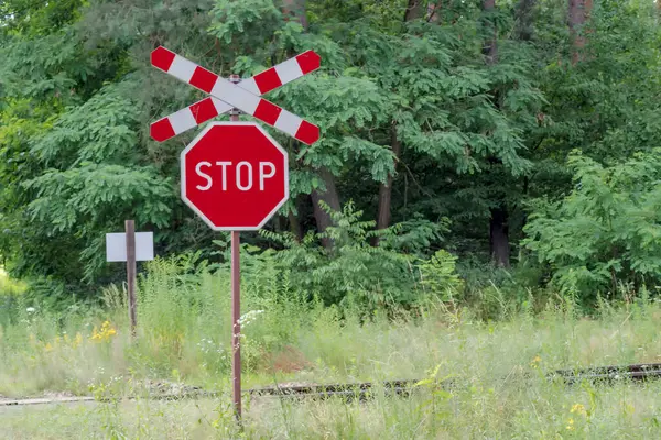 Stop sign on the road. Road sign.Stop sign and Saint Andrew s cross - railway crossing in the forest. A forest railway line among lush trees on a July afternoon.