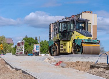 Poland Ostrowiec Swietokrzyski April 12, 2024 at 12:11. AMMANN road roller on a road construction site. A large construction machine on a road construction site under a blue sky with clouds on the background of an apartment block.   clipart