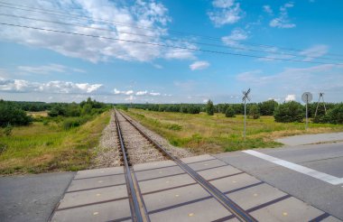Yazın güneşli bir havada yol. Demiryolu kavşağı. Mavi gökyüzünün altında orman ve çayırlar boyunca uzanan izler. Ozarow 'un (Swietokrzyskie Voyvodeship) kenarında, doğa arasında güzel ve güneşli bir yaz öğleden sonra) . 