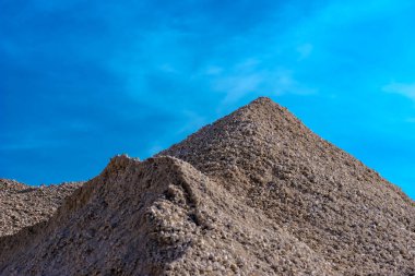 Mavi bir arka planda kum ve çakıllar. Mavi gökyüzü arka planında resim gibi görünen bir çakıl yığını. Nisan 'ın sonlarında güzel bir yay gökyüzünün altındaki bir yol inşaatında inşaat malzemeleri deposu..   