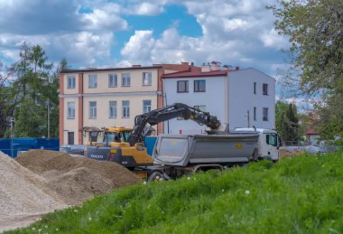 Polonya Ostrowiec Swietokrzyski, 26 Nisan 2024, saat 11: 15. Bir Volvo kazıcısı bir çöp kamyonuna çakıl yüklüyor. Yol inşaatının üzerinde beyaz bulutlar olan mavi gökyüzü. İsveç yapımı bir kazıcı, bir çöp kamyonuna çakıl döker..  