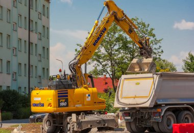  Polonya Ostrowiec Swietokrzyski 25 Mayıs 2024, saat 12: 20. Komatsu kazıcısı toprağı yol inşaatındaki bir çöp kamyonuna yüklüyor. Şehirde apartman blokları arasında bir bölüme bir yol inşa ediliyor. Toprak işleme sırasında Japon kazıcısı .  