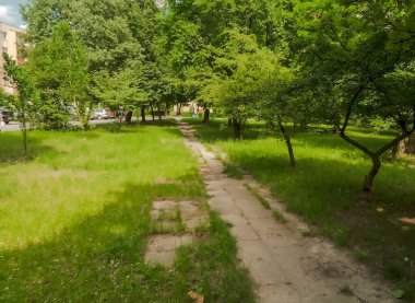 Parktaki çimenlikte yeşil çimenler, bahçedeki ev. Şehrin yeşil bölgelerinde bir yürüyüş yolu. Apartman bloklarının arasında küçük bir park. Şehir parkındaki çimlere uzanan beton levhalardan yapılmış bir yol..  