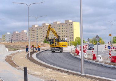 Yeni yol inşaatı. Polonya Ostrowiec Swietokrzyski 22 Nisan 2024 saat 11: 31 'de. Bir yol inşaatında Komatsu kazıcısı. Bir grup işçi, Japon bir kazıcının yardımıyla yeni bir yol boyunca (ve kaldırım) bir çimen seriyor..  