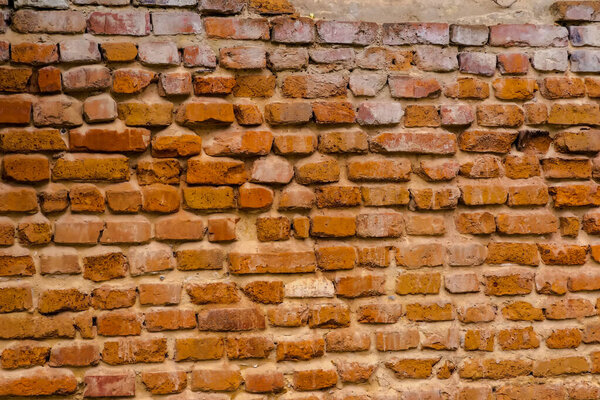 Red brick wall texture. An old wall made of red brick damaged (by time and weather). The brick wall of a ruined building has been worn away by the teeth of time .  