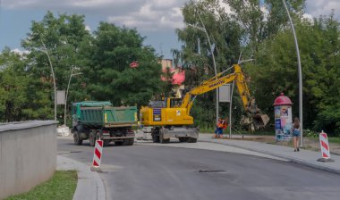 Polonya Ostrowiec Swietokrzyski 18 Temmuz, 2024 saat 22: 10 'da kentte yeni bir karayolu inşaatı - KOMATSU kazıcı faaliyet halinde. Japon sarı kazıcı (mürettebatlı) yol inşaatındaki kaldırım inşaatına son rötuşları yapıyor.. 
