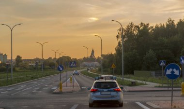 Gün batımında otoyolda arabalar, trafik ışıkları, arabalar, trafik ışıkları, yol ve trafik işaretleri. Gün batımında şehir sokaklarında bir polis arabası. Şehir (Ostrowiec Swietokrzyski) bir yaz akşamında, batan güneş tarafından resmedilmiştir.. 
