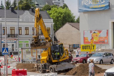 Poland Ostrowiec Swietokrzyski July 12, 2024 11 14 am. KOMATSU excavator working on a road construction site.Japanese yellow excavator digs earth at a road construction site in the city among historical buildings . clipart