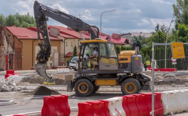Büyük bir inşaat sahası bir kazıcıyla çalışıyor. Koparka Volvo prauje na placu budowy drogi przy budowie ronda. İsveçli kazıcı tamamen yeniden inşa edilmiş bir sokak üzerinde yoğun bir şekilde bir kavşak (döner kavşak) inşası üzerinde çalışıyor. 