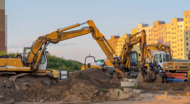  Poland Ostrowiec Swietokrzyski September 3, 2023 5:46 p.m. LIEBHERR and HYUNDAI excavators on a road construction site at sunset. Wheeled excavators and one crawler excavator at sunset on a road construction site in the city among apartment blocks.  clipart