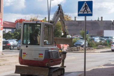 Road sign in the city.Poland Ostrowiec Swietokrzyski October 16, 2024 at 1:40 p.m. TAKEUCHI crawler excavator, carries WACKER compactor . A small Japanese excavator driving down a city street is heading to a job site near on a sunny autumn day.   clipart