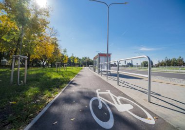 Toplu taşıma durağı ve sonbahar ağaçlarının önünde asfalt yüzeyi olan bir bisiklet yolu, kentte yeni inşa edilmiş ve yeni hizmete sokulmuş, içinde sonbahar çevresindeki OSTROWIEC SWITOKRZYSKI adlı bir otobüs durağı bulunan yeni bir yol.
