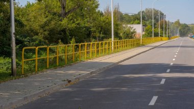 Şehirdeki yol. Sarı çelik bariyer kaldırımı eski sanayi kanalından koruyor. Eski çelik fabrikasından geçen yol - şu anda şehrin sanayi sonrası bir bölgesidir (Ostrowiec). 