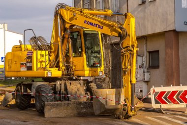  Polonya Ostrowiec Swietokrzyski 27 Kasım 2024, saat 12: 29 'da KOMATSU kazıcı faaliyete geçti. Bir Japon kazıcı, sonbahar güneşinin ışığında tarihi evlerin yenilendiği bir sokakta duruyor.. 