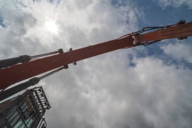 Bulutlu mavi gökyüzüne karşı kazıcının çalışan kolu. Büyük bir kazıcının çalışan kolu, bir bahar sabahı bulutlu bir gökyüzünün arka planına doğru uzanıyordu..  